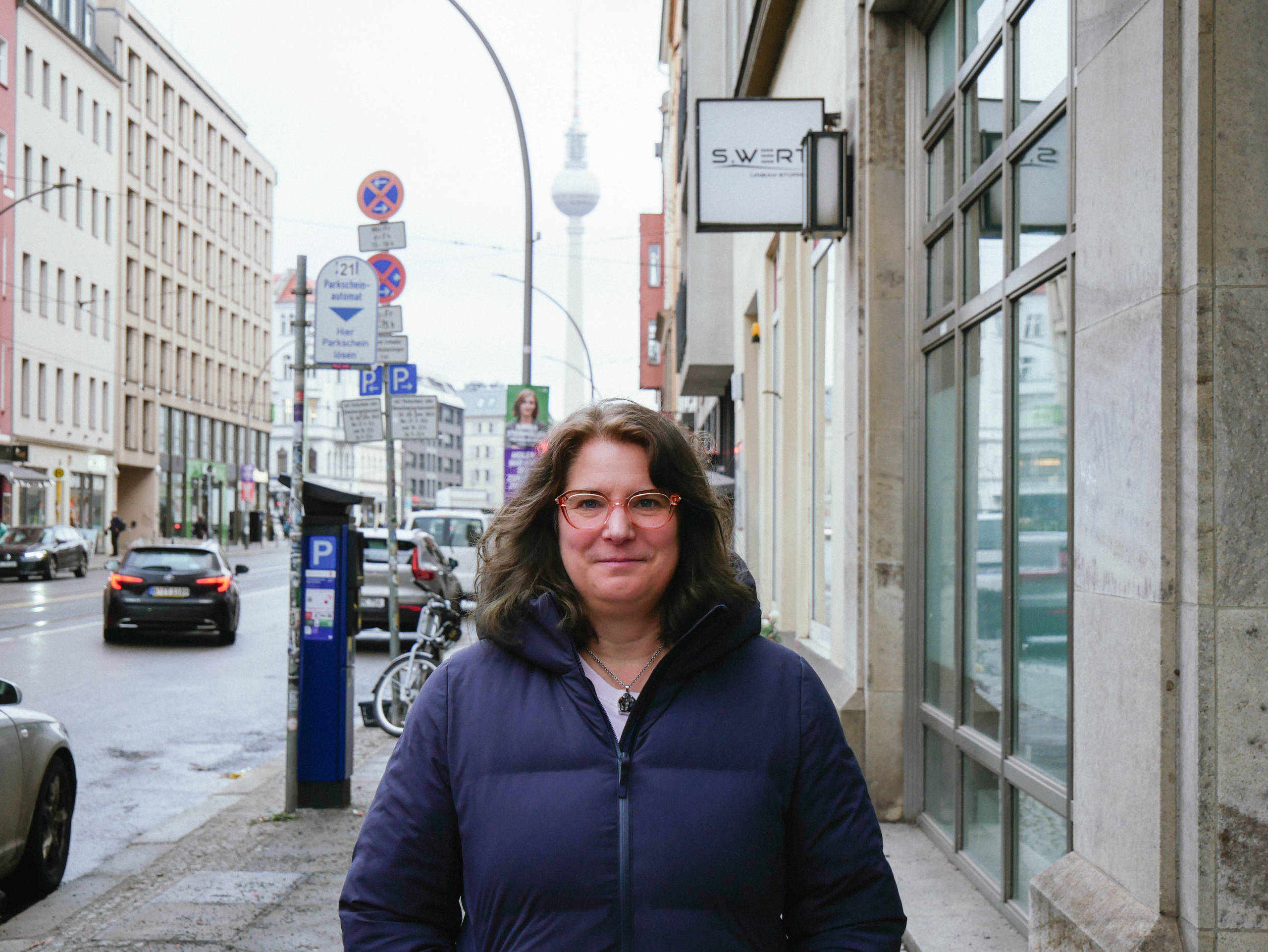 Porträt einer Frau mit Brille und dunkler Jacke, im Hintergrund der Fernsehturm von Berlin